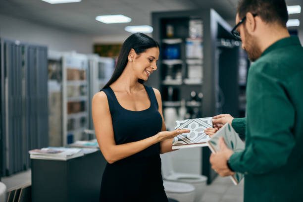 A smiling female seller recommends ceramic tiles for a male customer, at the home design shop.